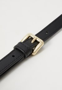 Cintura in pelle nera con una fibbia dorata, caratterizzata da una superficie liscia e una cucitura visibile, con un piccolo logo impressato sulla pelle.
