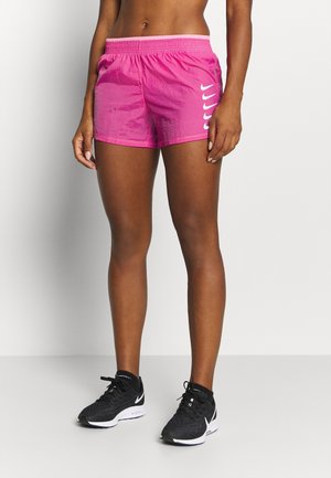 Fit persoon draagt felroze sportshorts met meerdere witte Nike Swoosh-logo's op het linkerbeen en zwarte Nike hardloopschoenen.