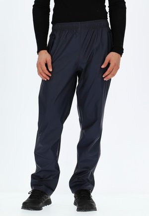 Navy waterproof trousers with elastic waistband, side pockets, tapered design, and smooth texture, paired with black athletic shoes.