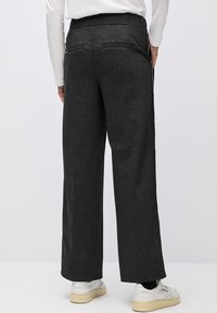 Weit geschnittene, dunkelgraue Hose mit einer weichen Textur, ausgestattet mit zwei Gesäßtaschen und kontrastierenden seitlichen Streifen. Getragen mit weißen Sneakern.