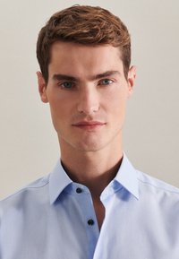 Camicia a maniche lunghe di colore azzurro chiaro con colletto a punta, caratterizzata da bottoni scuri e una texture di tessuto liscia. Ritratto ravvicinato di un modello.