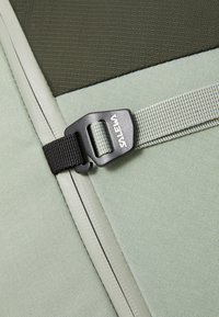 Lys grønn stoff med en teksturert finish, med en svart plastspenne og grå webbingreim; vinklet design med kontrasterende kanter.