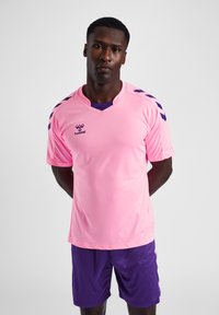 Rosa Sporttrikot mit V-Ausschnitt und lila Akzenten, mit kurzen Ärmeln und Hummel-Logo, kombiniert mit lila Shorts.