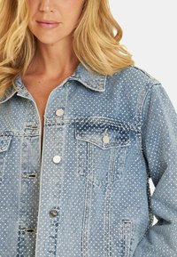 Veste en denim de couleur bleu clair, ornements en pois, col classique, poches à rabat à l'avant et accessoires en métal argenté.