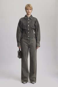 Denim odijelo u pranom crnom sadrži usku jaknu s velikim džepovima, širokim rukavima i ravnim hlačama. Drži malu torbicu.
