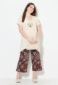 Beige, tuniek met korte mouwen en een V-hals, voorzien van een decoratieve zak; gecombineerd met donkere, met bloemenpatroon bedrukte, wijde broek. Beige gestructureerde clutch en schoenen.