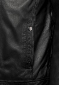 Zwarte leren jas met een gladde textuur, zijzakken met metalen drukknoopjes en zichtbare stiksels langs de naden.