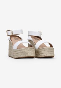 Sandalias de cuña blancas con suela de yute trenzado, tira al tobillo y diseño de punta abierta. La plantilla es color beige con un sutil logotipo en la plantilla.
