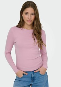 Langärmliges pinkes Oberteil mit Rundhalsausschnitt, enganliegendem Design und weicher Textur, getragen mit blauen Jeans. Verfügt über eine glatte Oberfläche und moderaten Stretch.