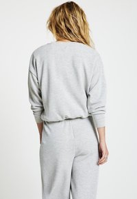 Completo felpa e pantaloni grigi in tessuto morbido, caratterizzato da una vestibilità rilassata e cintura elasticizzata, con maniche lunghe e scollo rotondo.