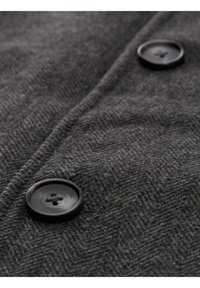 Tela de espiga gris con una textura suave, que presenta dos botones negros de diseño circular y cuatro orificios cada uno.