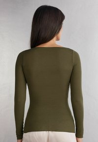 Langsleeve top in olijfgroen, gemaakt van aansluitende stof. Kenmerkt zich door een vierkante halslijn en een gladde textuur, met een licht gebogen zoom aan de achterkant.
