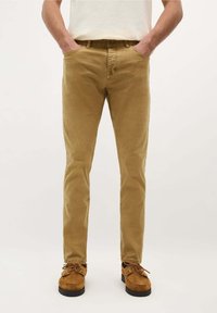 Pantalons en coton slim-fit, couleur fauve, avec poches avant, jambes droites, et une texture subtile, associés à des chaussures en daim marron.