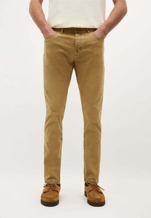 Pantalons en coton slim-fit, couleur fauve, avec poches avant, jambes droites, et une texture subtile, associés à des chaussures en daim marron.
