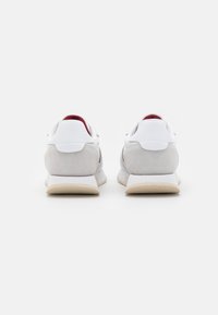 Zapatillas blancas y grises con un talón de ante, suela de goma plana, parte superior de malla y forro interior rojo, que presentan un diseño minimalista.