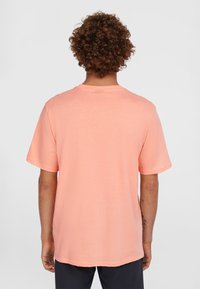 Kortærmet t-shirt i lys ferskenfarve, med et enkelt design og rund hals, blød tekstur og afslappet pasform, der har en lige kant.