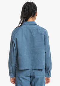 Blue corduroy jacket with a cropped design, featuring a pointed collar, long sleeves, and subtle vertical ribbed texture.