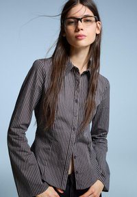 Striped button-up shirt in dark gray with light gray vertical stripes, featuring a classic collar, long flared sleeves, and button details.