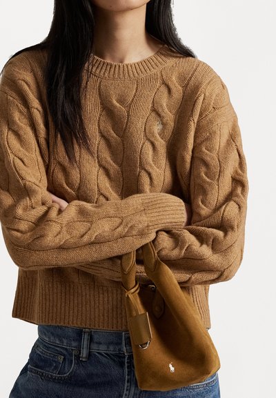 Suéter marrón de punto trenzado con un cuello redondo acanalado, combinado con un pequeño bolso de ante beige que presenta un acento de logo. Jeans de mezclilla visibles.