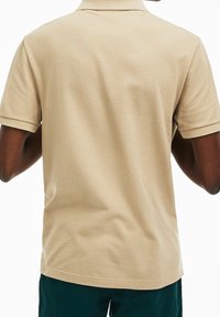 Polo de color beige hecho de algodón texturizado, con mangas cortas, cuello y dobladillo recto. Diseño minimalista sin marcas visibles.