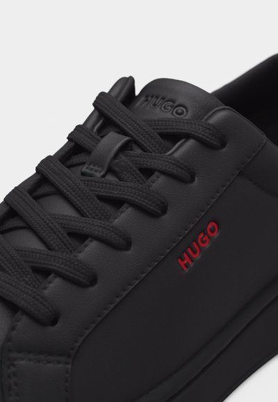 Baskets en cuir noir avec lacets noirs, logo "HUGO" en relief sur la languette, et logo "HUGO" rouge sur le côté.