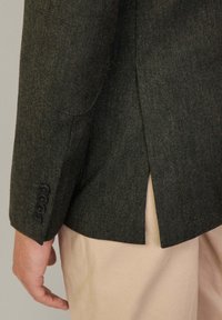 Blazer verde con motivo a spina di pesce, dotato di apertura laterale, dettaglio con tre bottoni sui polsini e vestibilità su misura, realizzato in tessuto testurizzato.