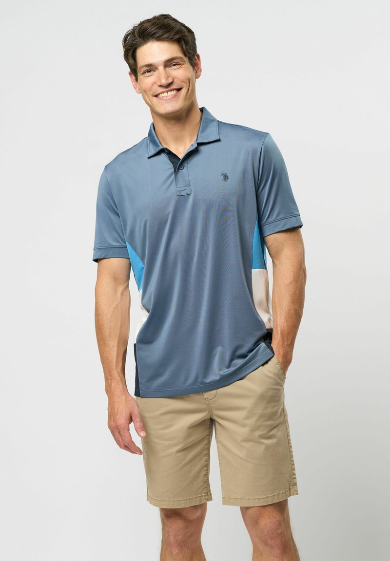 Men's polo shirt in blue and light blue, short sleeves, textured fabric with a logo on the chest; paired with light beige shorts.