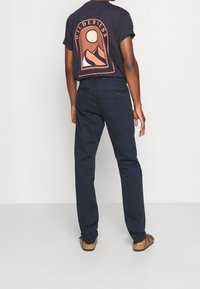 Pantaloni di cotone blu navy con tasche posteriori, abbinati a una maglietta nera con una grafica colorata di montagna e sole sul retro.