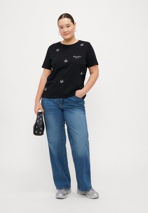 T-shirt nera in cotone a maniche corte, con design geometrici argentati; abbinata a jeans di denim azzurro chiaro e sneakers grigie.