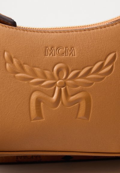 Superficie in pelle marrone con logo MCM in rilievo e design di alloro sotto una zip dorata.