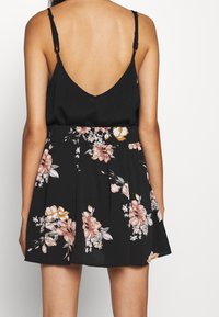 Robe noire à fleurs avec un dos en forme de V, une taille élastiquée et une jupe évasée ornée de motifs floraux roses et jaunes.