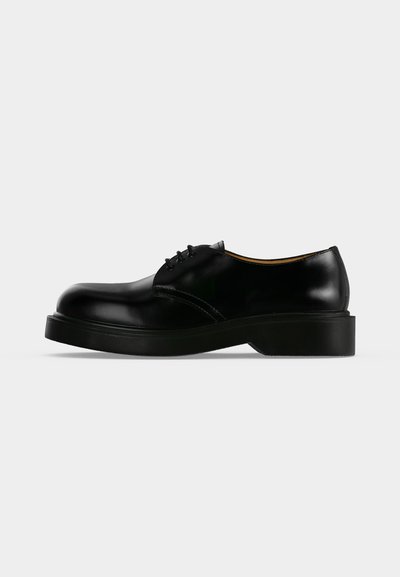 Chaussure de ville noire en cuir poli à lacets, avec une semelle épaisse, un bout arrondi et un petit talon, montrée de profil sur un fond uni.
