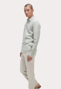 Camisa de lino color verde claro, de botones y mangas largas, y pantalones de lino beige. Diseño simple con un ajuste relajado y cuello plano. Estética minimalista.