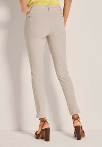 Beige Slim-Fit-Hosen mit glatter Textur, verfügen über zwei aufgesetzte Taschen auf der Rückseite und eine mittelhohe Taille, kombiniert mit braunen Absatzsandalen.
