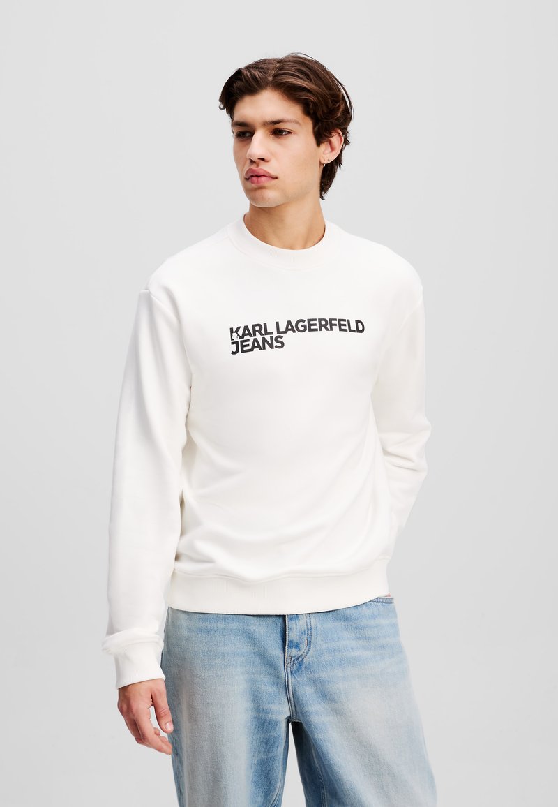 Fehér pulóver, kerek nyakkal, a mellkason fekete "KARL LAGERFELD JEANS" logóval. Puha anyag és bordás ujjak.