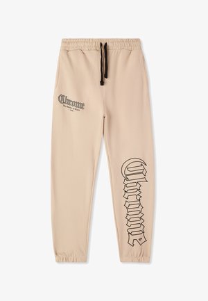 Pantaloni jogging beige con cintura elastica, cordoncino nero e grande testo nero stampato sul lato. Tessuto morbido e liscio.