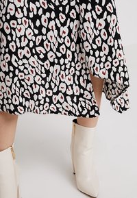 Černé šaty s bílým a červeným leopardím vzorem. Mají volný střih s asymetrickým lemem a jsou kombinovány s bílými kotníkovými botami.