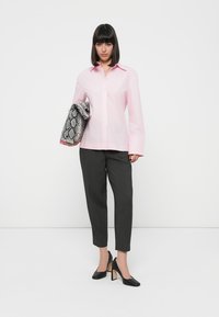 Lys rosa skjorte med lange ermer, sammen med grå smale bukser og svarte høyhælte sko. Holder en mønstret clutch.