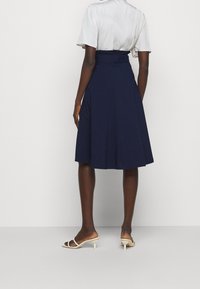 Gonna plissettata blu navy con vita belted, realizzata in tessuto morbido, presenta un taglio al ginocchio e una texture liscia. Indossata con sandali leggeri.