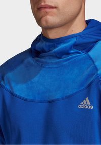 Felpa sportiva blu con cappuccio, tessuto testurizzato e design a pannelli contrastanti. Logo Adidas in argento sul davanti.