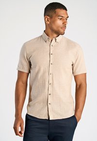 Korte mouw knoophemden in lichtbeige, gemaakt van textuurstof met een subtiele weving. Voorzien van knoopkraag en donkere knopen.