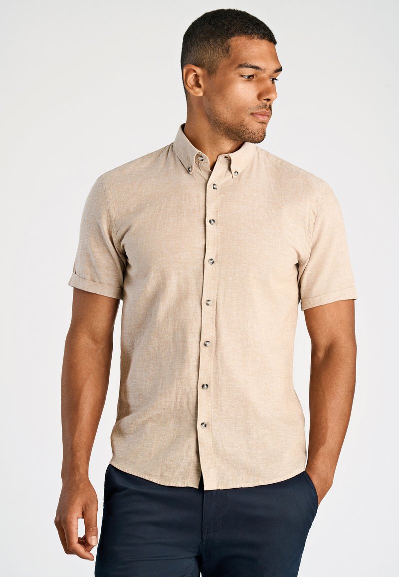 Korte mouw knoophemden in lichtbeige, gemaakt van textuurstof met een subtiele weving. Voorzien van knoopkraag en donkere knopen.