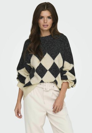 Striktrøje i sort og creme med en diamantmønster. Oversize pasform med ribbede mansjetter og kant, båret over lyse bukser.