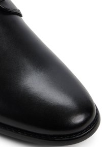 Zapato de cuero negro con una textura suave, diseño de punta afilada y costuras sutiles a lo largo del borde. Sin acentos de hardware visibles.