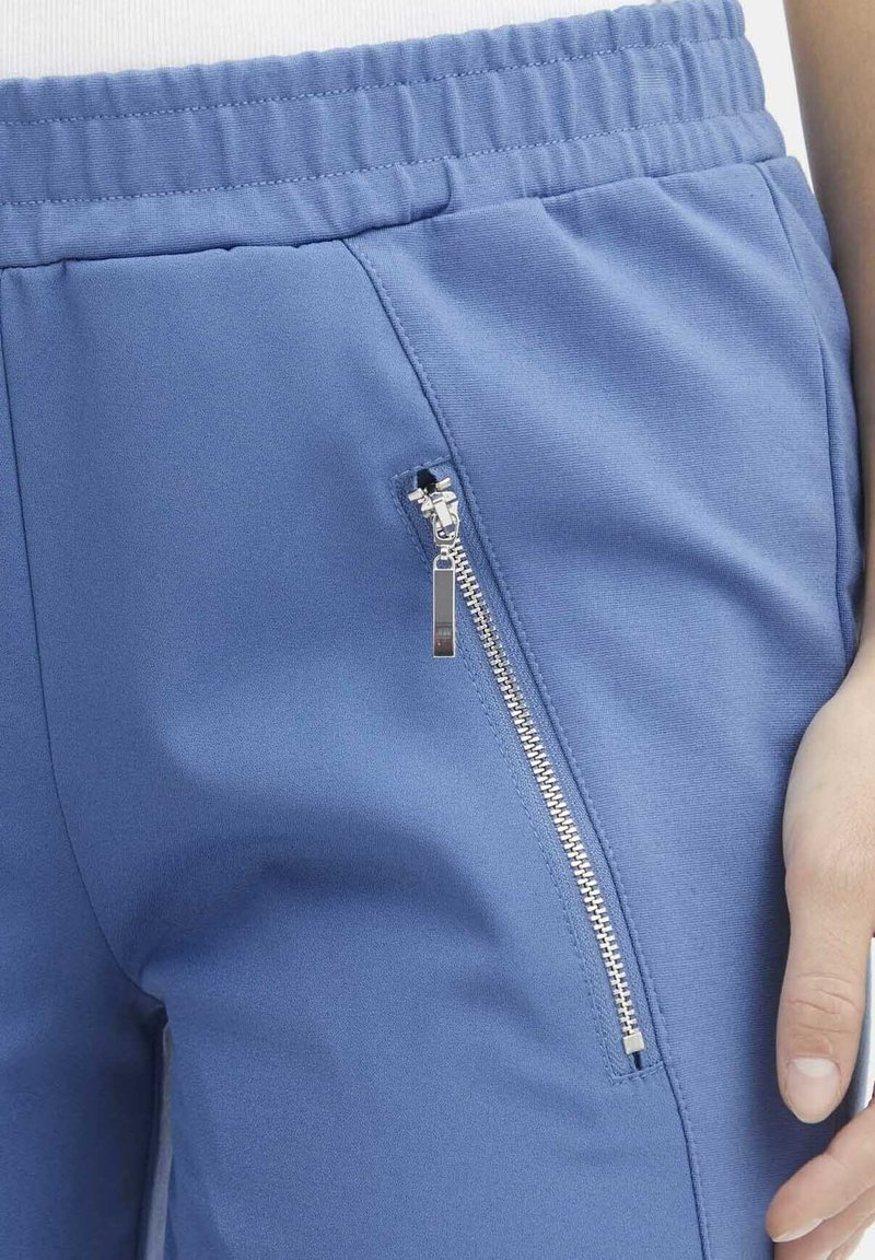 Pantalons de sport bleus en matière douce avec une taille élastique, dotés d'une poche zippée sur le côté et d'une texture lisse.