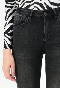 Jeans negros de cintura alta con una silueta ajustada, que presentan costuras en tono, cinco bolsillos y una sutil textura desgastada.