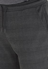 Black drawstring pants with a textured check pattern, featuring side pockets and a relaxed fit for comfort and versatility.