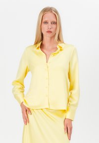 Yellow satin long-sleeve shirt with a collared neckline, front button closure, and a relaxed fit. Smooth texture and slightly cropped design.