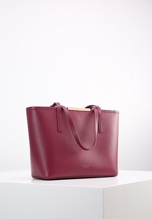 Bolso tote de cuero burdeos con doble asa y sutil logotipo de marca en relieve, descansando sobre un pedestal blanco.