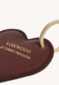 Porte-clés en cuir bordeaux en forme de cœur avec l'inscription dorée "LOXWOOD LE CABAS PARISIEN" et un attachement en métal doré.